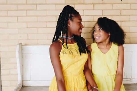 two girls siting on a white bench in yellow dress